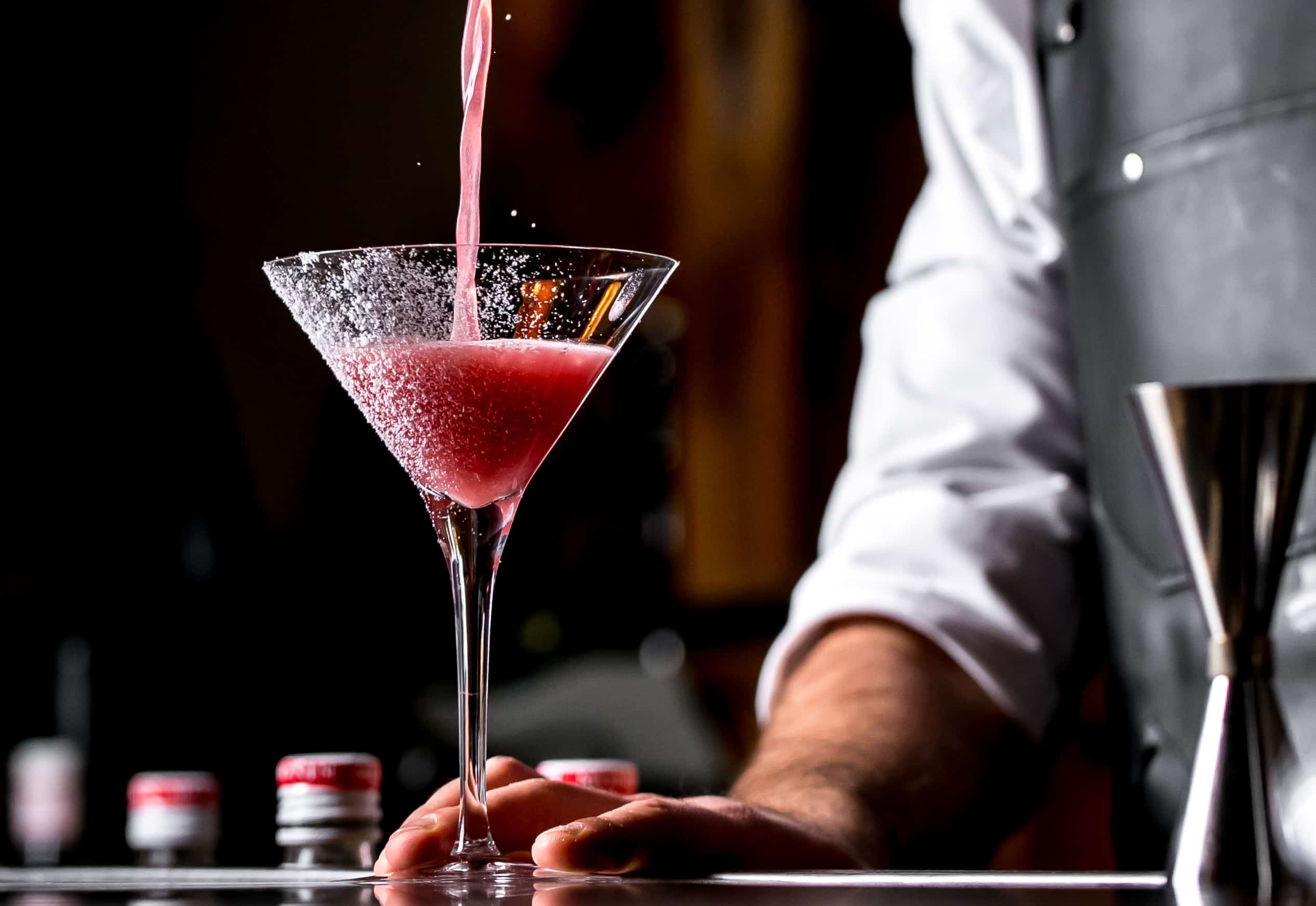 bar tender pours cocktail from cocktail shaker into martini glass